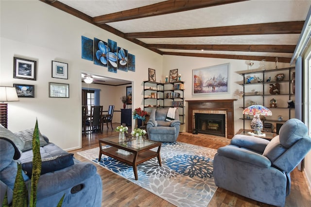 living area with a ceiling fan, a fireplace, vaulted ceiling with beams, and wood finished floors