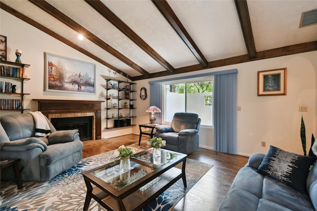 living area with wood finished floors, visible vents, a fireplace with raised hearth, baseboards, and vaulted ceiling with beams
