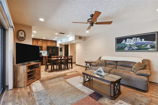 living room with a textured ceiling, baseboards, ceiling fan, and light wood-type flooring