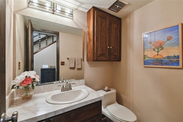 half bath featuring toilet, vanity, a textured ceiling, visible vents, and a textured wall