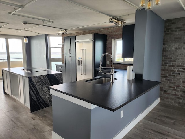 kitchen featuring a sink, dark wood finished floors, brick wall, built in fridge, and dark countertops