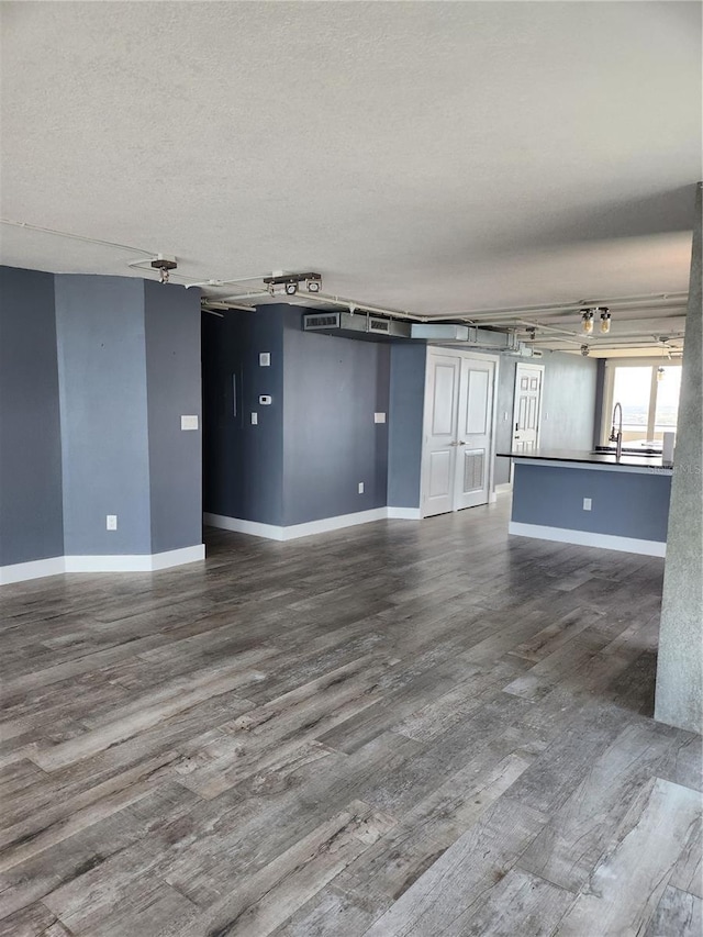spare room with a sink, a textured ceiling, baseboards, and dark wood-style floors
