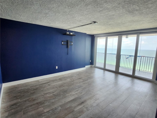 empty room featuring a textured ceiling, a water view, baseboards, and wood finished floors