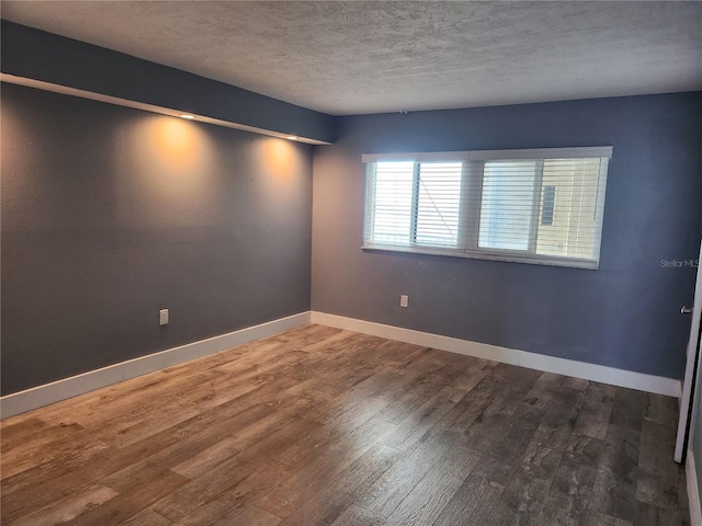 spare room with baseboards, a textured ceiling, and wood finished floors
