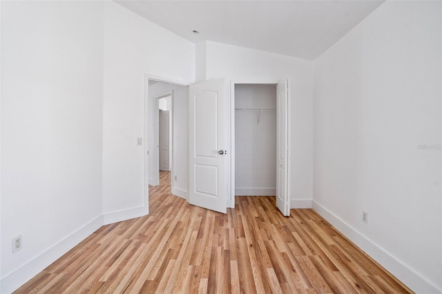 unfurnished bedroom featuring vaulted ceiling, light wood finished floors, baseboards, and a closet