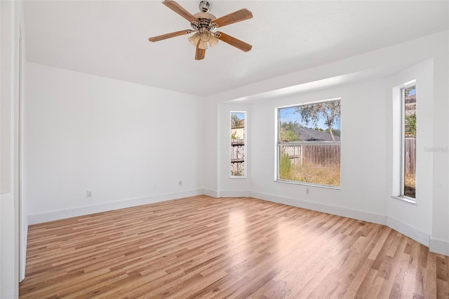 empty room featuring light wood finished floors, baseboards, and a ceiling fan