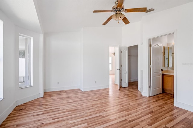 unfurnished bedroom featuring multiple windows, light wood-style floors, ensuite bathroom, and a walk in closet
