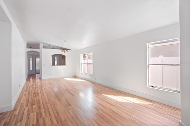 unfurnished living room featuring vaulted ceiling, light wood-style flooring, baseboards, and arched walkways