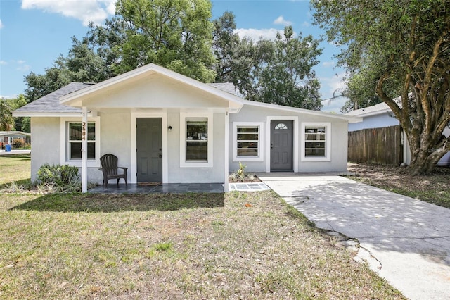 bungalow-style home with stucco siding, fence, a front lawn, a shingled roof, and a porch