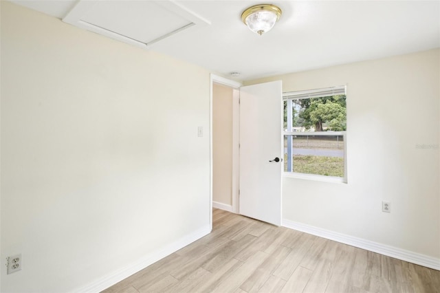 empty room with attic access, light wood-style floors, and baseboards