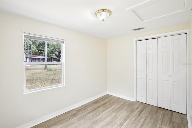 unfurnished bedroom featuring a closet, attic access, baseboards, visible vents, and light wood-type flooring