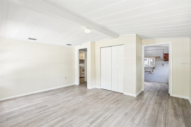 unfurnished bedroom with a closet, baseboards, light wood finished floors, visible vents, and lofted ceiling with beams