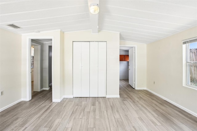 unfurnished bedroom featuring a closet, light wood-style floors, visible vents, and vaulted ceiling with beams