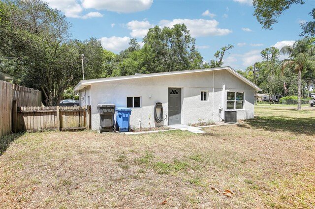 rear view of property featuring a lawn, cooling unit, stucco siding, and fence