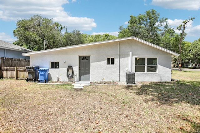 rear view of house featuring central air condition unit, stucco siding, fence, and a lawn