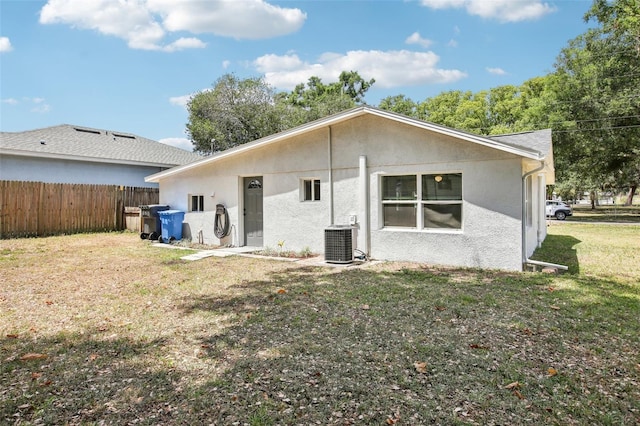 rear view of property with central air condition unit, a yard, stucco siding, and fence