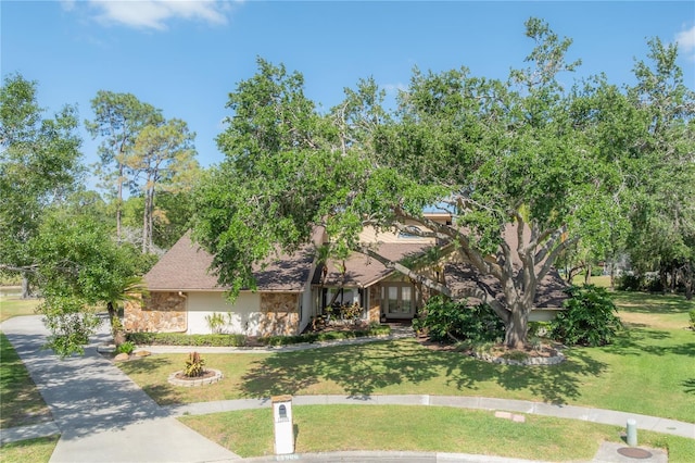 view of property hidden behind natural elements featuring french doors, roof with shingles, a front yard, stone siding, and stucco siding