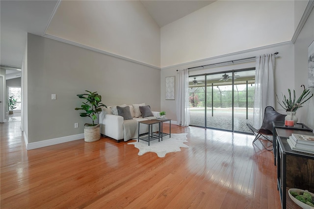 living area featuring a healthy amount of sunlight, high vaulted ceiling, baseboards, and light wood-style flooring