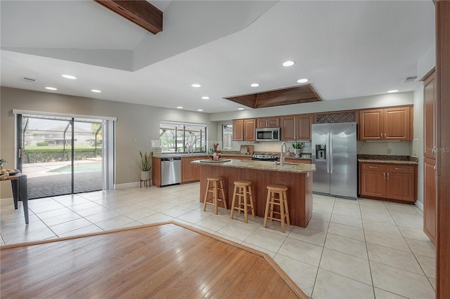 kitchen with a breakfast bar, light stone counters, an island with sink, stainless steel appliances, and baseboards