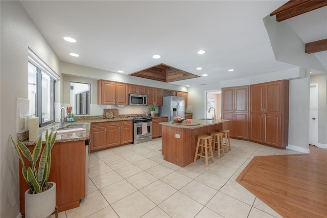 kitchen featuring light tile patterned floors, light stone counters, stainless steel appliances, and a kitchen bar