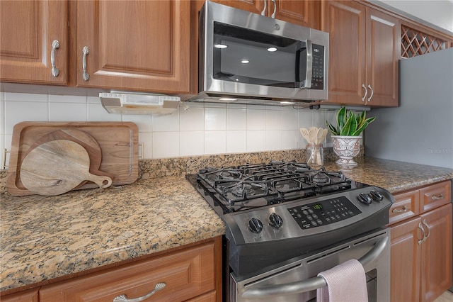 kitchen featuring appliances with stainless steel finishes, decorative backsplash, brown cabinetry, and light stone counters