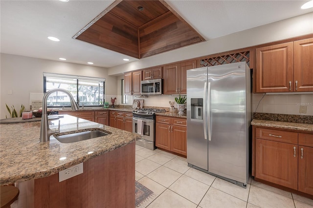 kitchen featuring stone counters, appliances with stainless steel finishes, brown cabinetry, and a sink