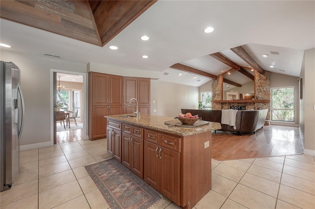 kitchen with light tile patterned floors, a sink, lofted ceiling with beams, stainless steel fridge, and a wealth of natural light