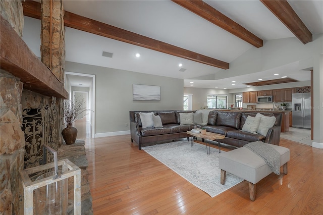 living area featuring baseboards, visible vents, lofted ceiling with beams, and light wood-type flooring