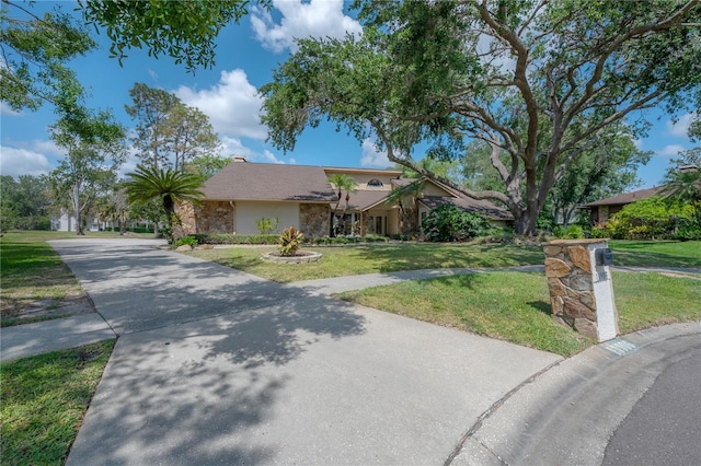 view of front facade featuring stucco siding, a front yard, stone siding, and concrete driveway