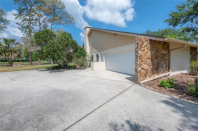 view of side of property featuring an attached garage, driveway, and stone siding