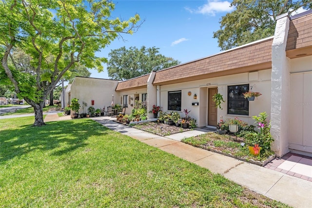 view of front of house featuring stucco siding, mansard roof, roof with shingles, and a front lawn
