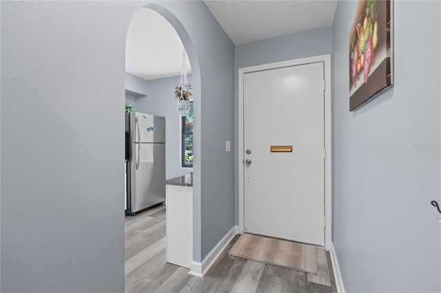 doorway with arched walkways, baseboards, and wood finished floors