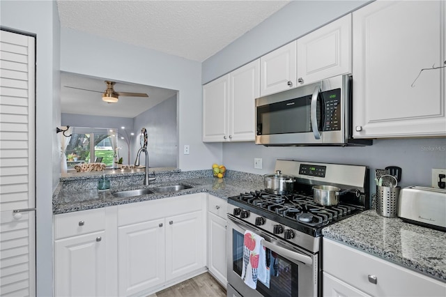 kitchen with a textured ceiling, white cabinets, a sink, stone counters, and stainless steel appliances