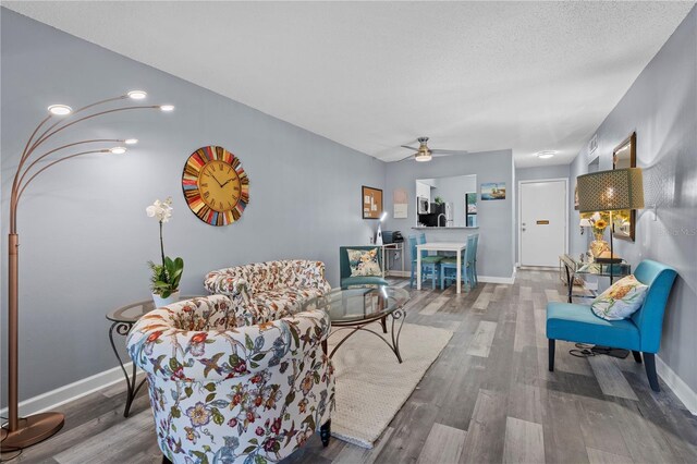 living area with baseboards, ceiling fan, and wood finished floors