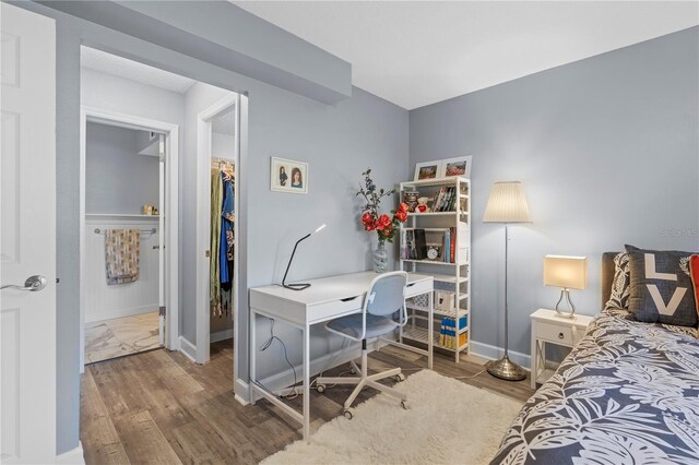 bedroom featuring baseboards, a walk in closet, wood finished floors, and a closet