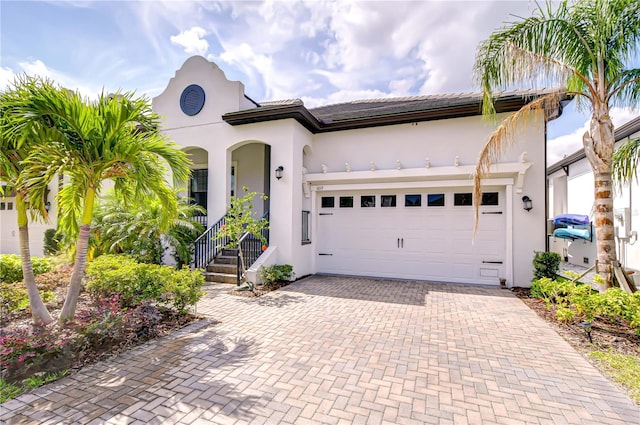 view of front of property featuring a tiled roof, decorative driveway, a garage, and stucco siding