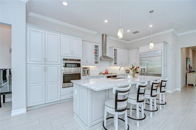 kitchen featuring light stone countertops, a sink, wall chimney exhaust hood, stainless steel appliances, and visible vents