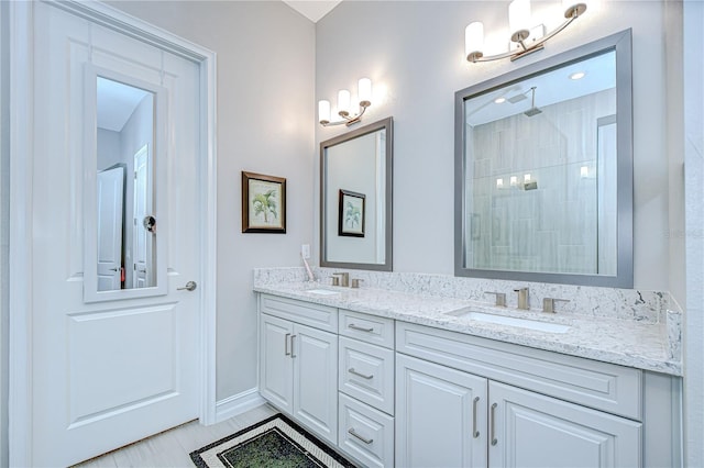 full bath featuring double vanity, baseboards, a tile shower, and a sink