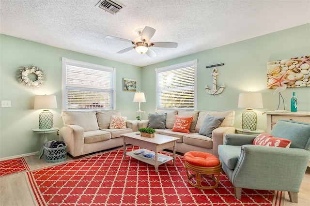 living area with visible vents, wood finished floors, baseboards, a textured ceiling, and a ceiling fan