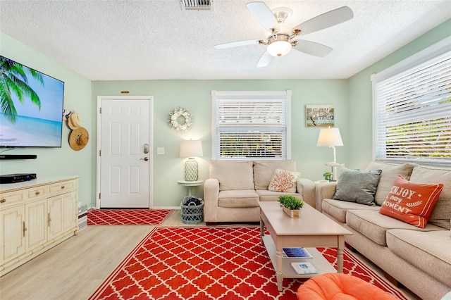 living area with visible vents, baseboards, ceiling fan, a textured ceiling, and light wood-style flooring