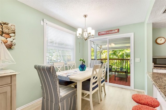 dining space featuring a textured ceiling, a chandelier, light wood-style flooring, baseboards, and visible vents