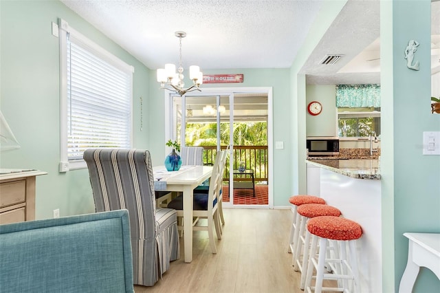 dining space featuring a textured ceiling, a chandelier, light wood-style flooring, baseboards, and visible vents