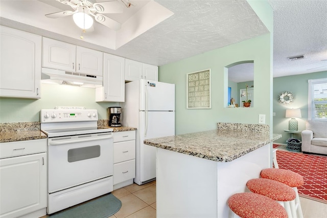 kitchen featuring white cabinetry, a breakfast bar, under cabinet range hood, and white appliances