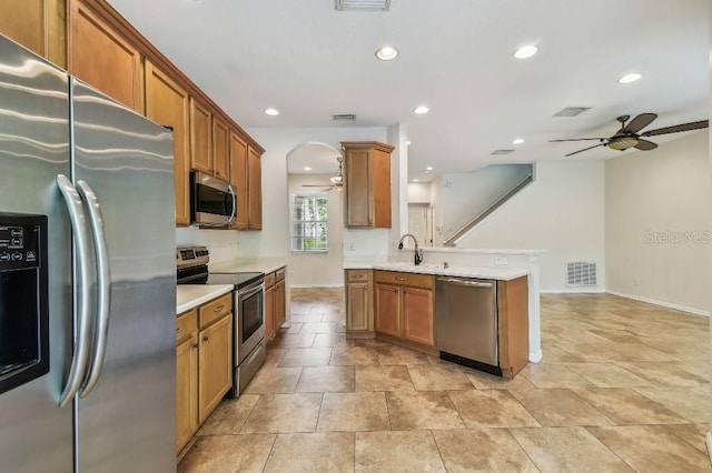 kitchen with stainless steel appliances, a ceiling fan, brown cabinetry, and a peninsula