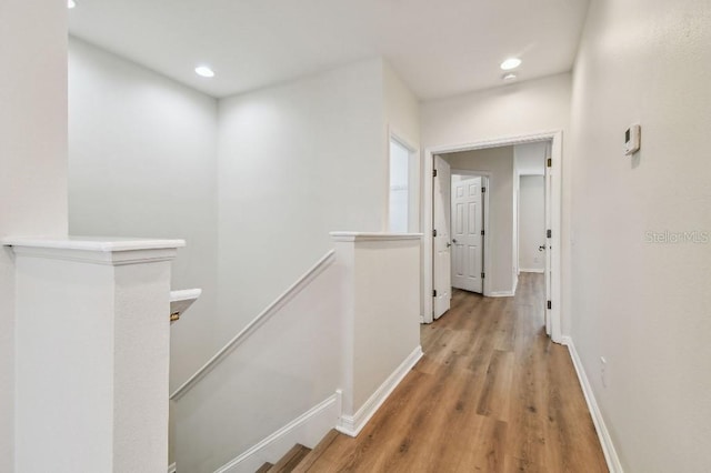 corridor with light wood-type flooring, recessed lighting, baseboards, and an upstairs landing