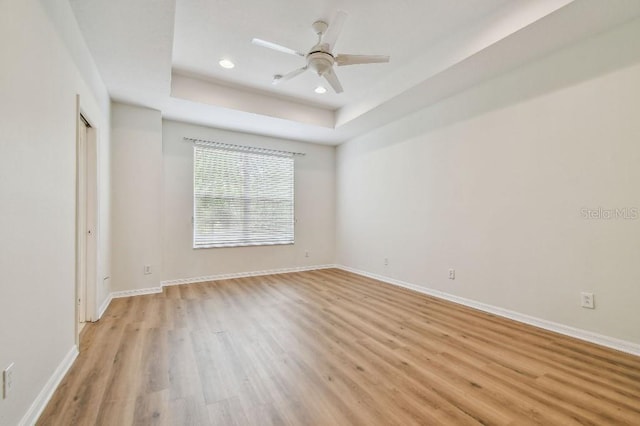 unfurnished room with a ceiling fan, light wood-type flooring, baseboards, a tray ceiling, and recessed lighting