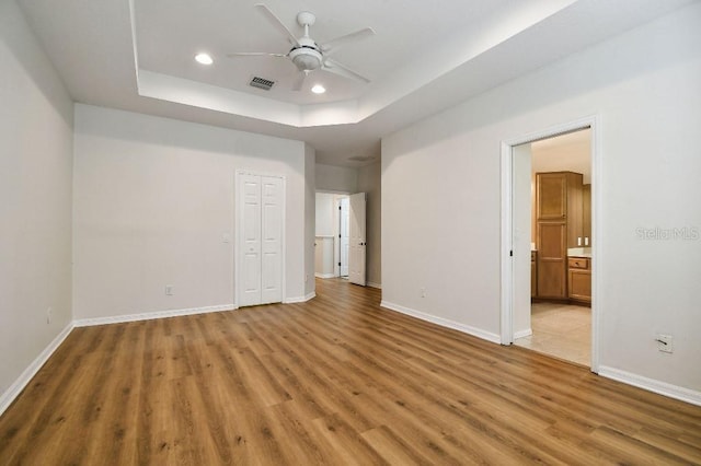 unfurnished bedroom featuring a tray ceiling, visible vents, baseboards, and light wood-type flooring