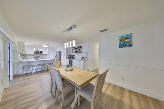 dining space with visible vents, light wood finished floors, and wine cooler