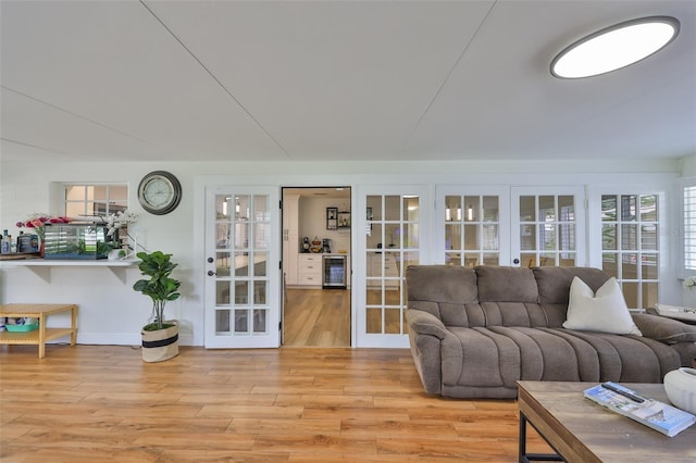 living area with beverage cooler, baseboards, french doors, and light wood-style flooring