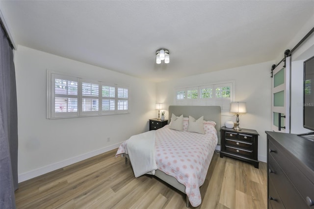 bedroom featuring baseboards, a barn door, and light wood finished floors